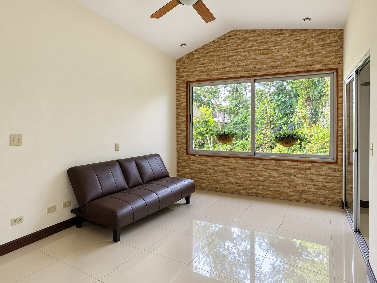 Room with a leather sofa and stone wall beside a garden window